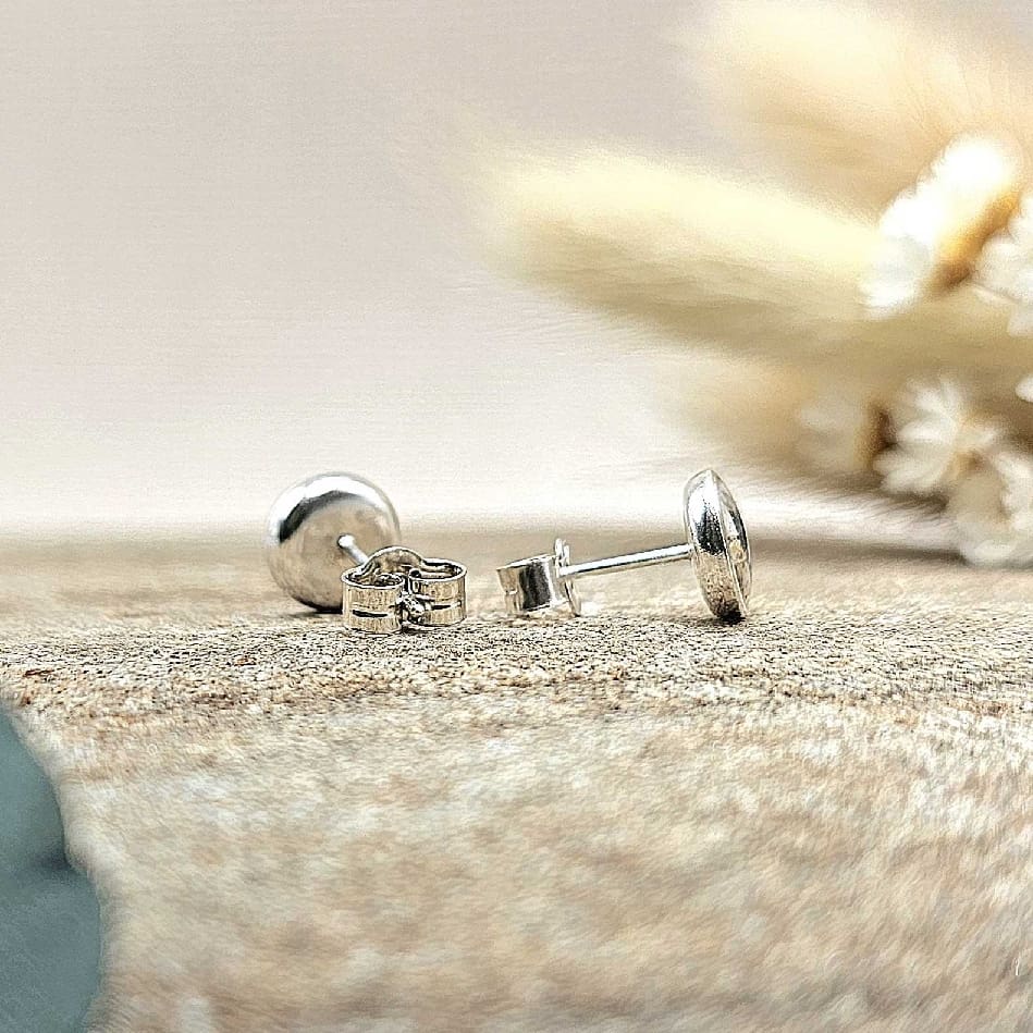 Displayed handmade tribute silver stud earrings facing away showing large butterfly push backs, with memento in clear resin