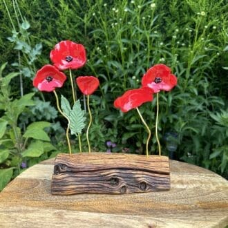 5 red resin poppies on gold wire set into a wooden log half. 3 poppies grouped on left, 2 on right.
