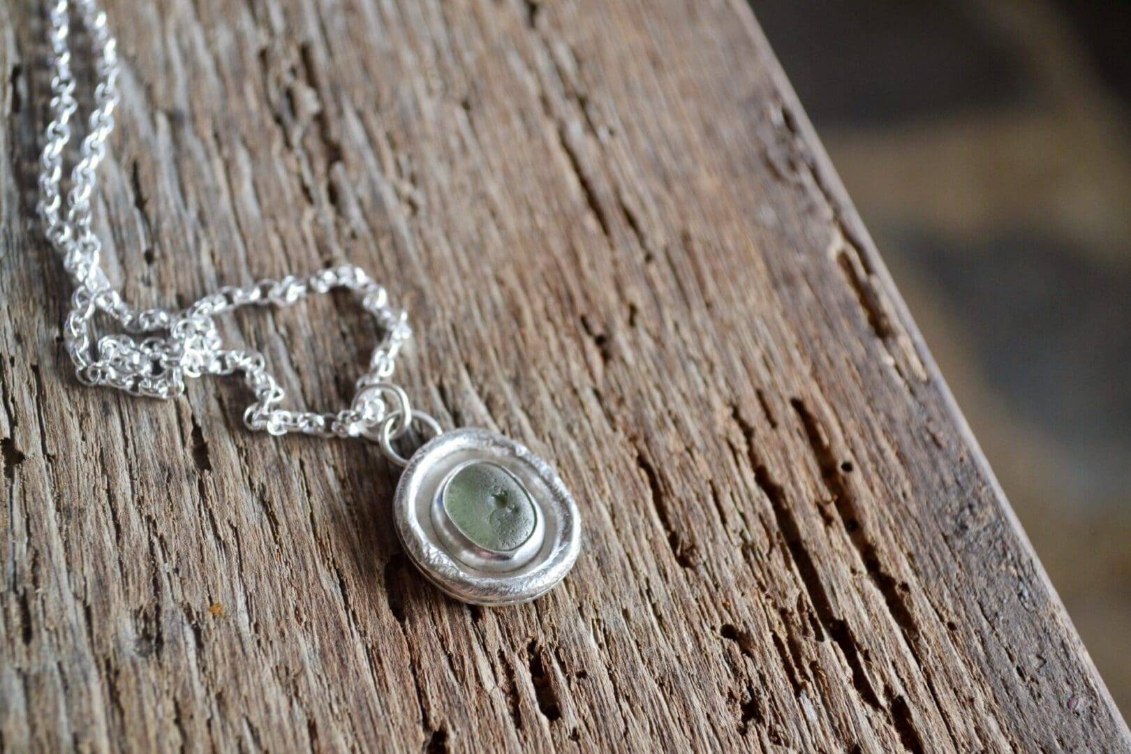 A silver necklace with molten texture on the pendant, which also has a piece of pale green sea glass