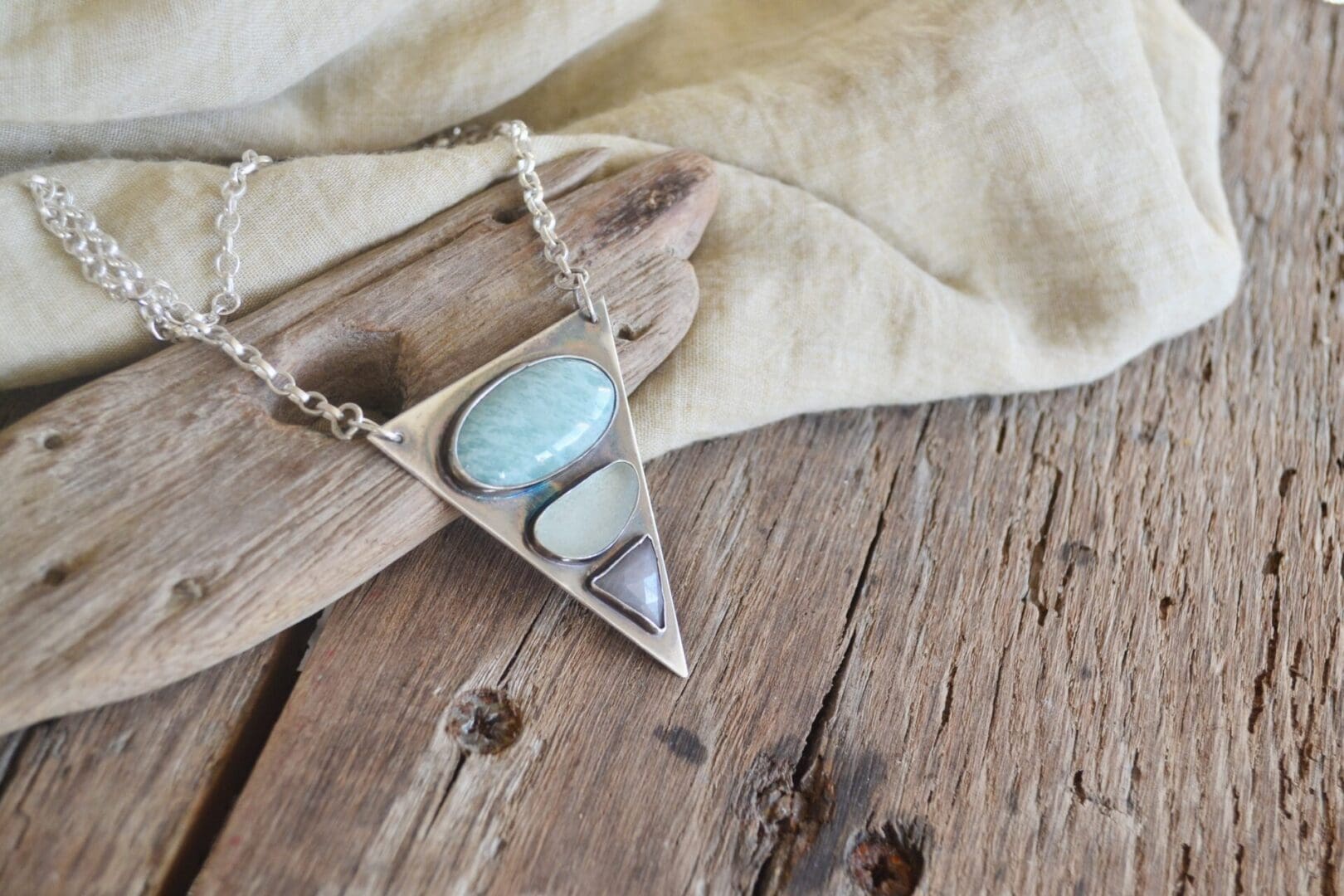 A triangular silver pendant with amazonite, sea glass and a triangular sapphire, on a silver chain attached by the top two corners