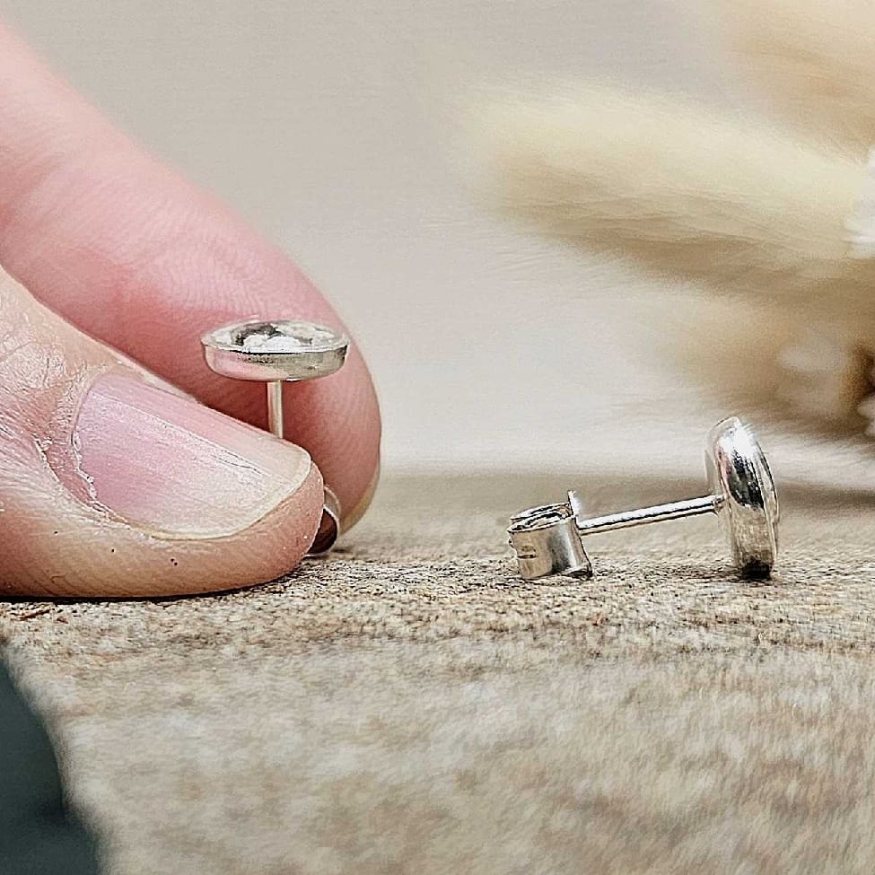 Jeweller's fingers holding upright a silver memorial stud earring. Second stud laying flat showing large butterfly push back