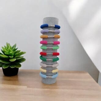 colourful chunky stackable bracelets show displayed on a stand that is on a light wooden countertop against a minimalist background.