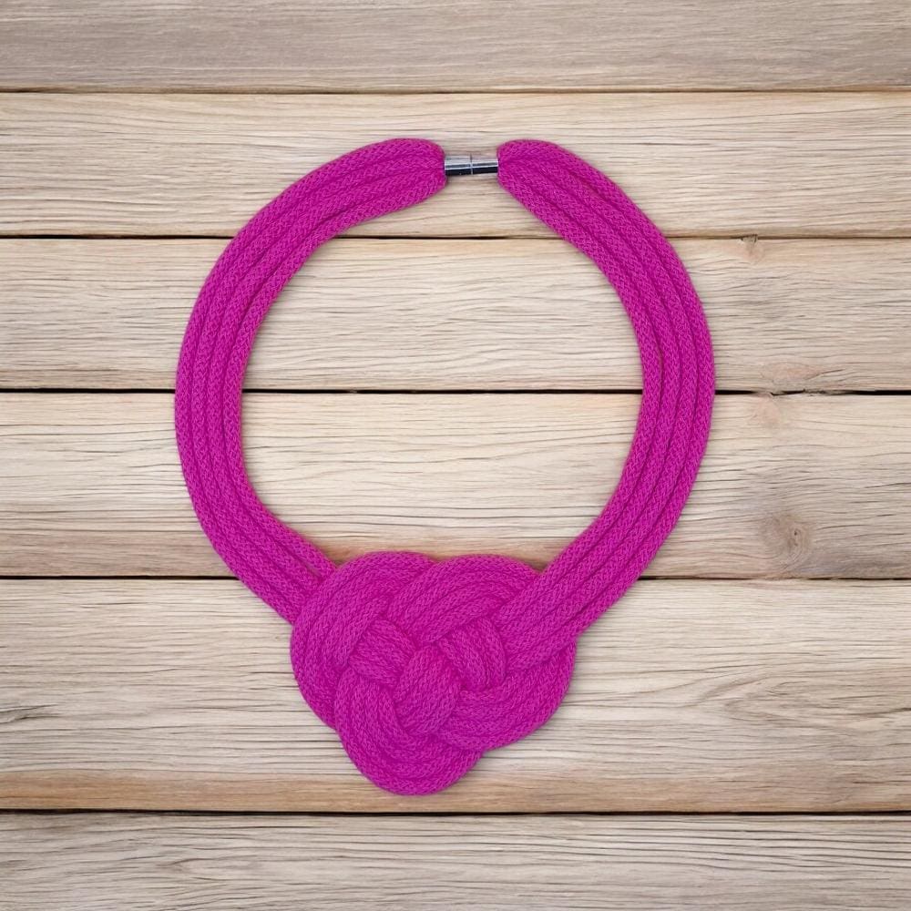 Modern pink chunky knotted cord necklace viewed from above against a pail wood floorboard background.