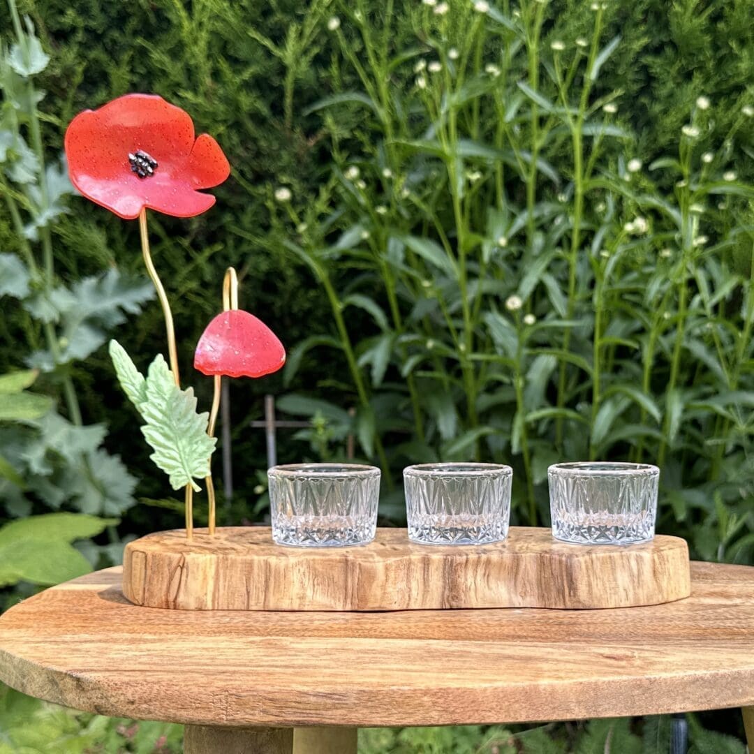 Wooden slice with 2 resin poppies on gold coloured wire with resin leaves attached. 3 round glass tealight holders sit on top of the wood slice