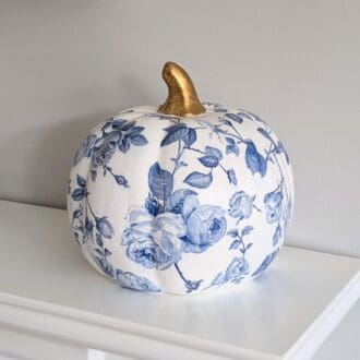 White ceramic pumpkin measuring 16,5cm decoupaged with a blue floral design and finished with a gold stalk.