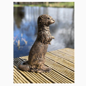 Realistic and detailed Bronze standing Otter sculpture by Kirsty Armstrong Sculpture next to a lake