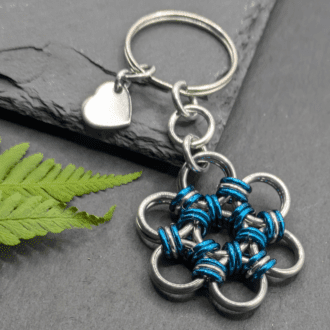 A keyring made into the shape of a flower. Made with larger silver rings and smaller dark teal and silver rings