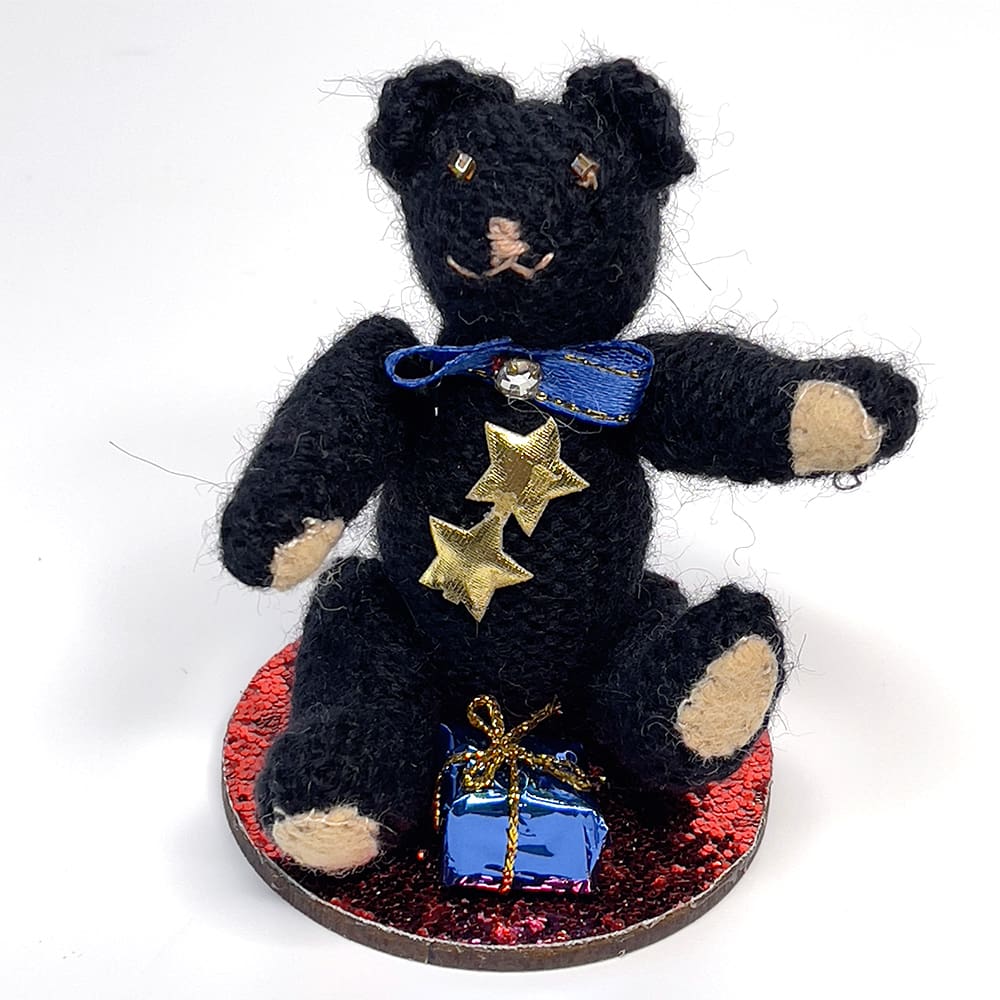 Miniature hand-knitted teddy bear in black wearing a blue bow tie Christmas decoration