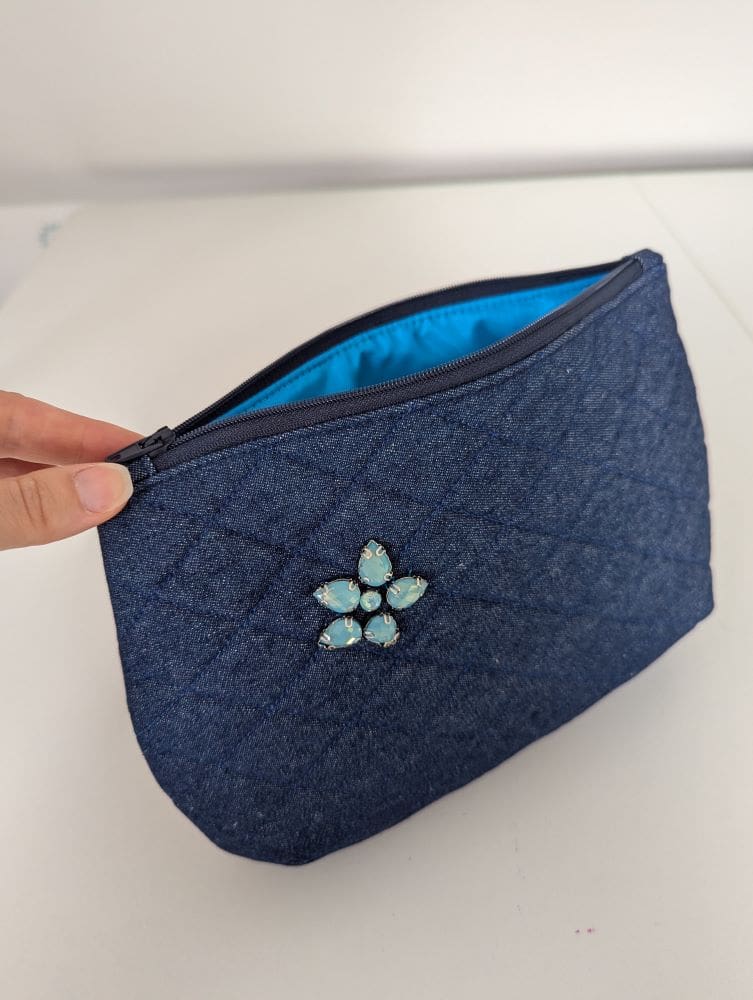 A denim pouch bag with turquoise lining and floral embellishment