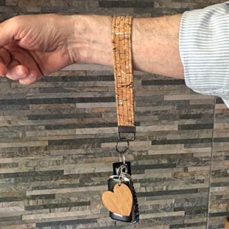 Natural cork key fob with keys attached, shown hanging from an arm against a narrow brick wall. Gunmetal split ring hardware.