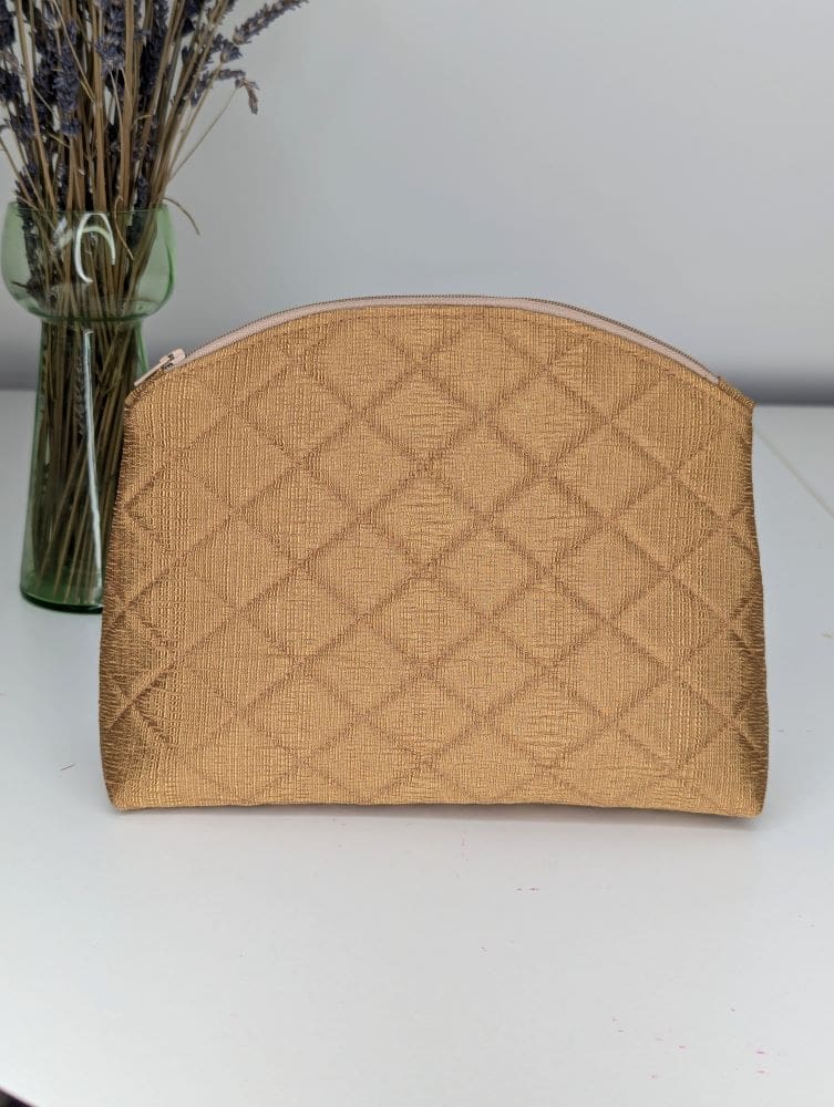 A quilted, gold make up bag with a rounded top edge