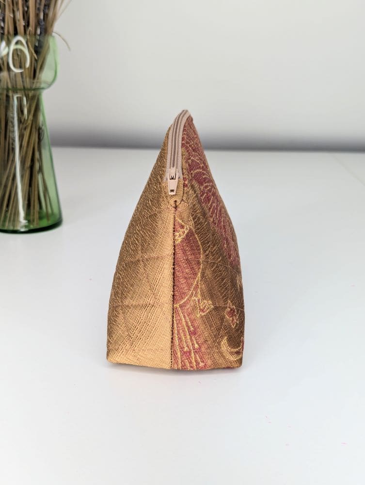 A handmade small zip pouch in gold and red, showing the side view, triangular shape