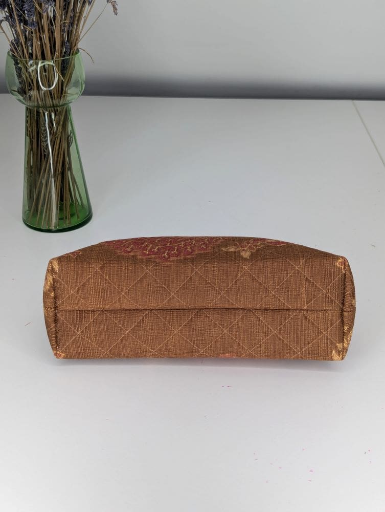 A medium size cosmetics bag shown laying down with the underside showing its width and depth