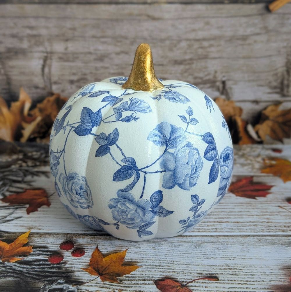 White ceramic pumpkin measuring 16,5cm decoupaged with a blue floral design and finished with a gold stalk.