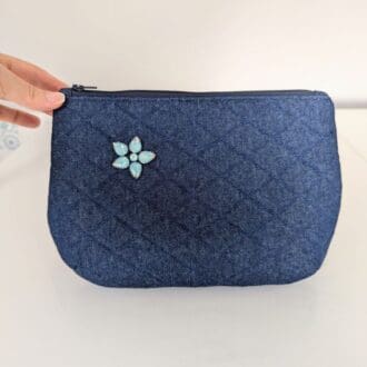 A quilted, denim clutch bag with a floral gemstone embellishment