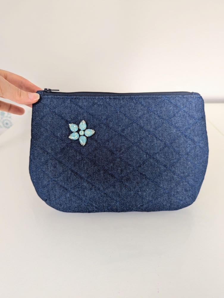 A quilted, denim clutch bag with a floral gemstone embellishment