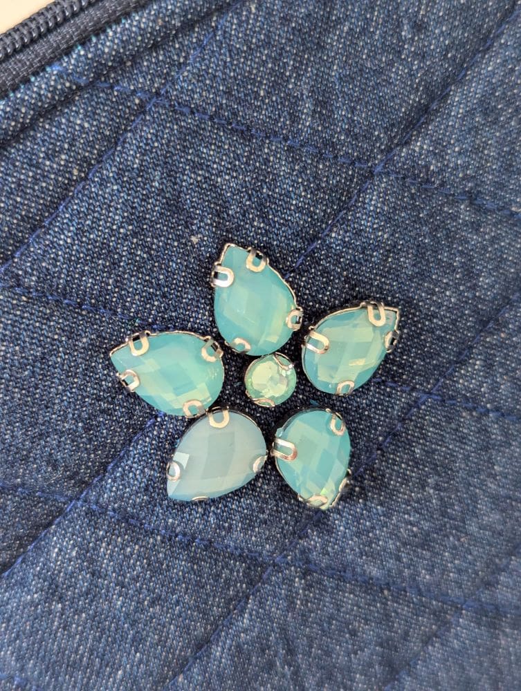 A small denim make up bag showing a close up of the turquoise gemstone embellishment