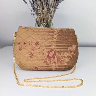 A gold coloured, quilted evening bag with a gold coloured copper chain with a deep red pleated lining