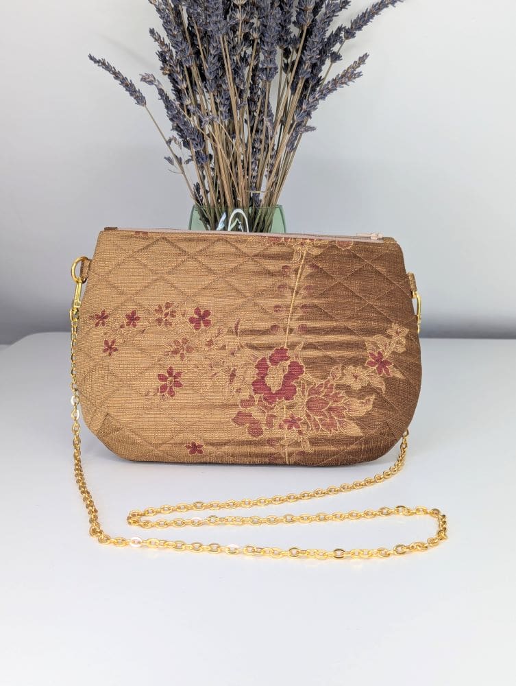 A gold coloured, quilted evening bag with a gold coloured copper chain with a deep red pleated lining