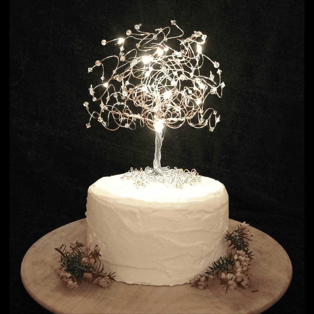 Fairly light wedding cake topper - silver wire tree, decorated with crystals and micro-lights sitting on top of an iced cake tier, decorated with heather.