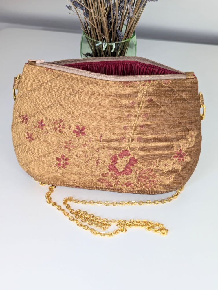 A gold coloured evening bag with a deep red lining and a gold coloured copper chain