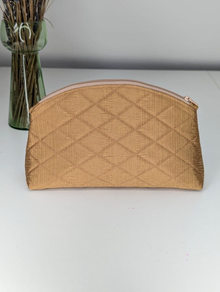 A handmade gold, quilted make up bag showing the back plain side on a white surface