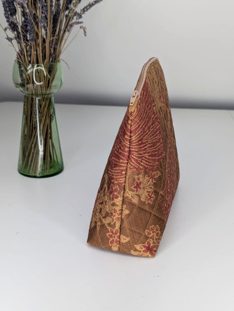 A gold and red wash bag shown from the side view on a white surface