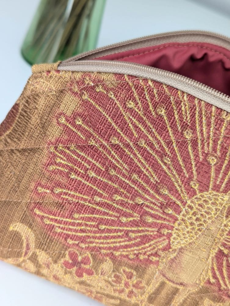 A close up view of a gold and red make up pouch, showing the quilting and zip fastening with a red lining