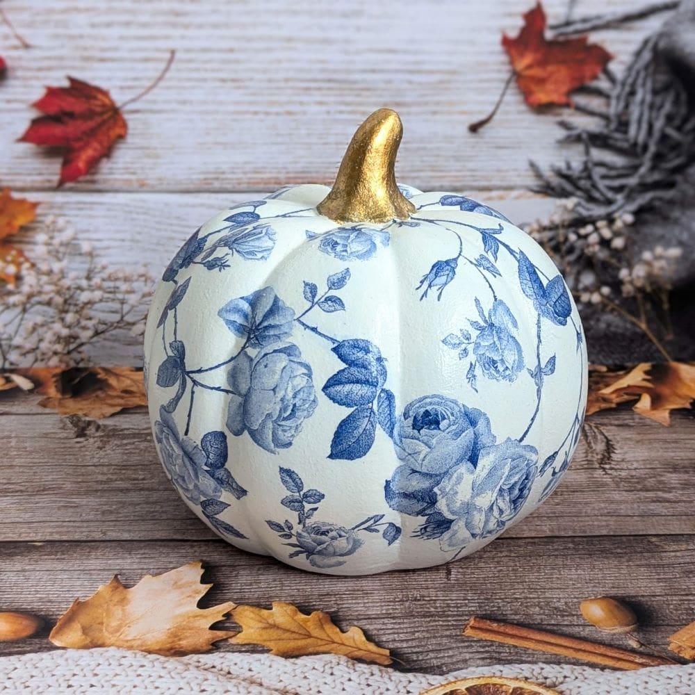 White ceramic pumpkin measuring 16,5cm decoupaged with a blue floral design and finished with a gold stalk.