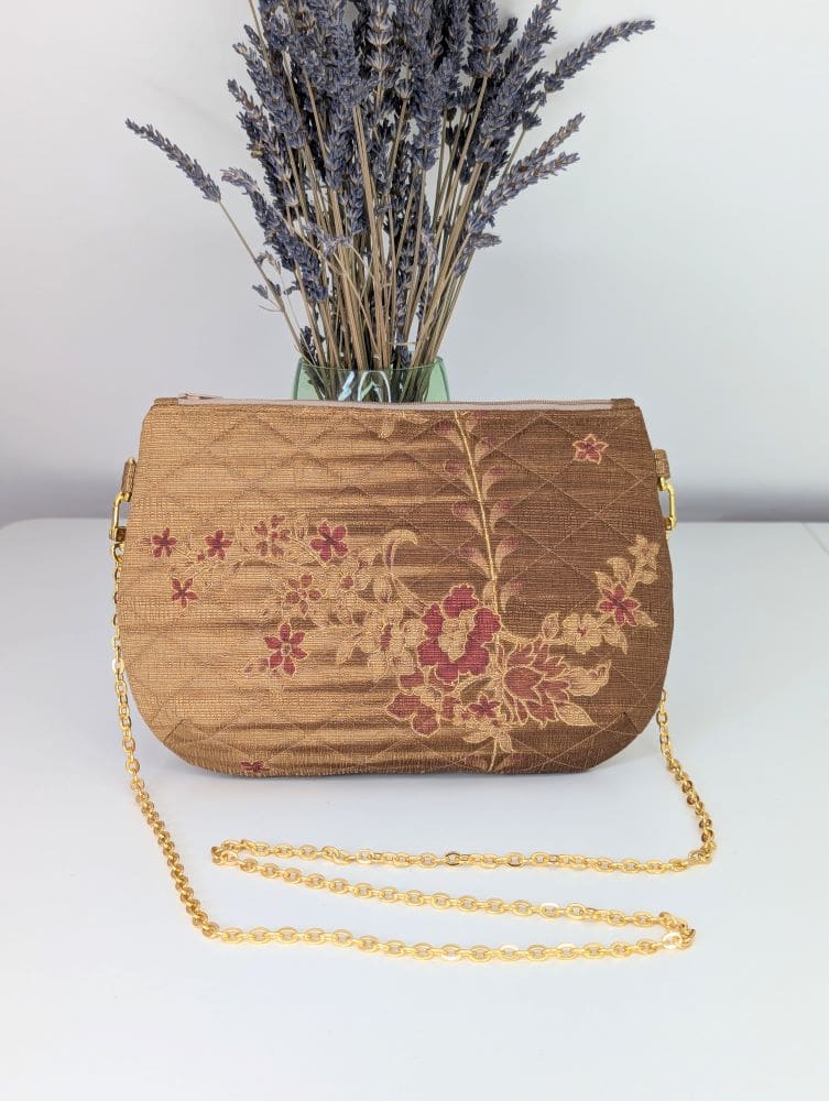 A handmade evening bag which is gold in colour, quilted and has a gold colour copper chain