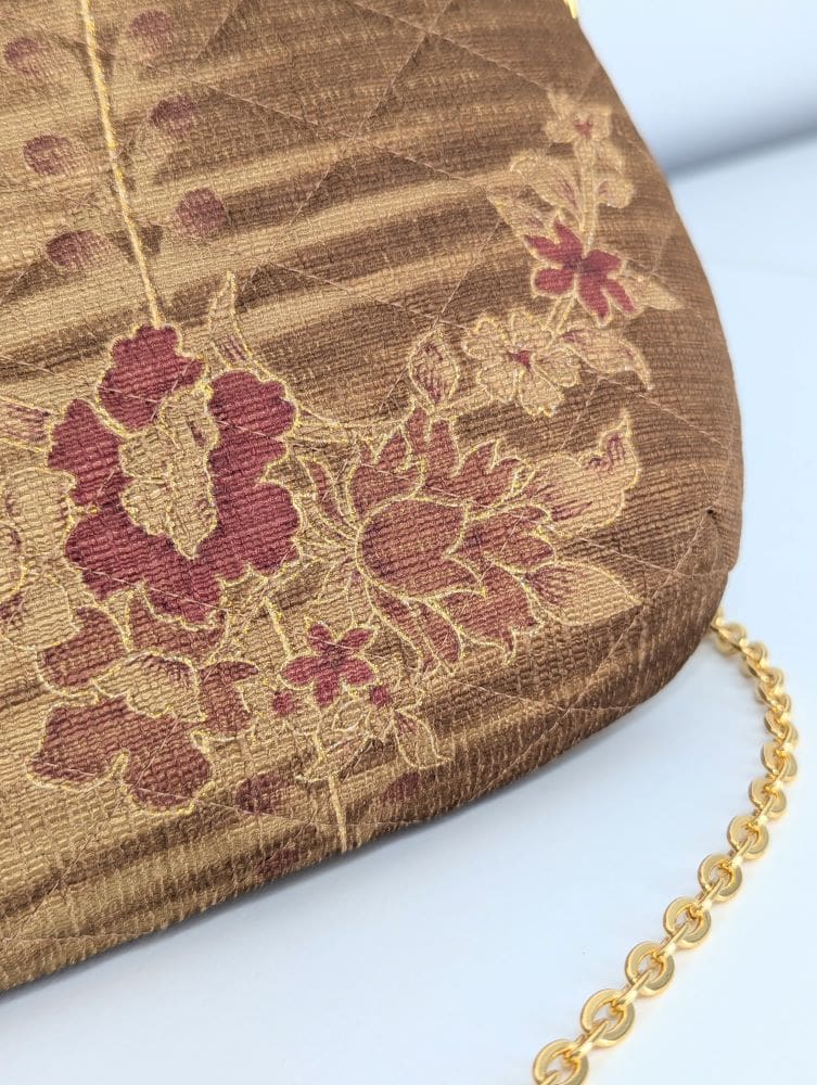 A close up view of the corner of a handmade quilted floral evening bag with a gold colour copper chain