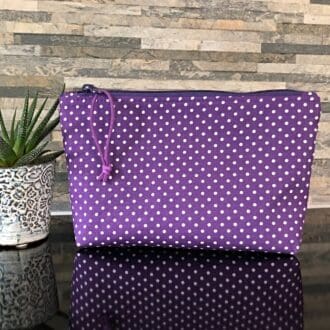 A medium-sized makeup bag featuring purple polka dot fabric, complemented by a purple zipper and lining.