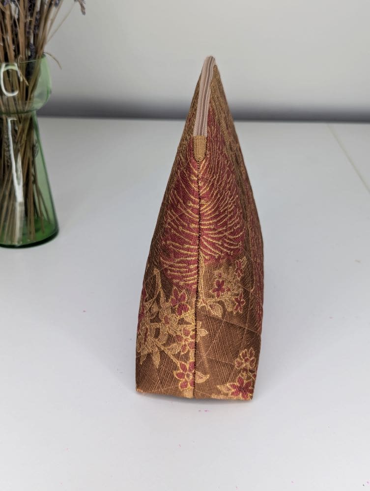 A medium size wash bag in gold and red shown from the side, indicating the triangular shape