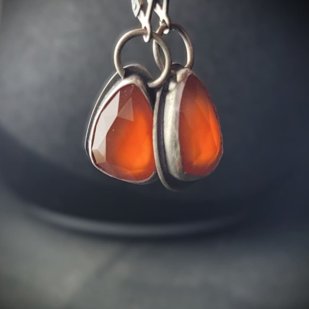 Orange Carnelian Faceted Cabochons in a raw oxidised sterling silver setting. In a teardrop shape with the back cut out to allow light through.