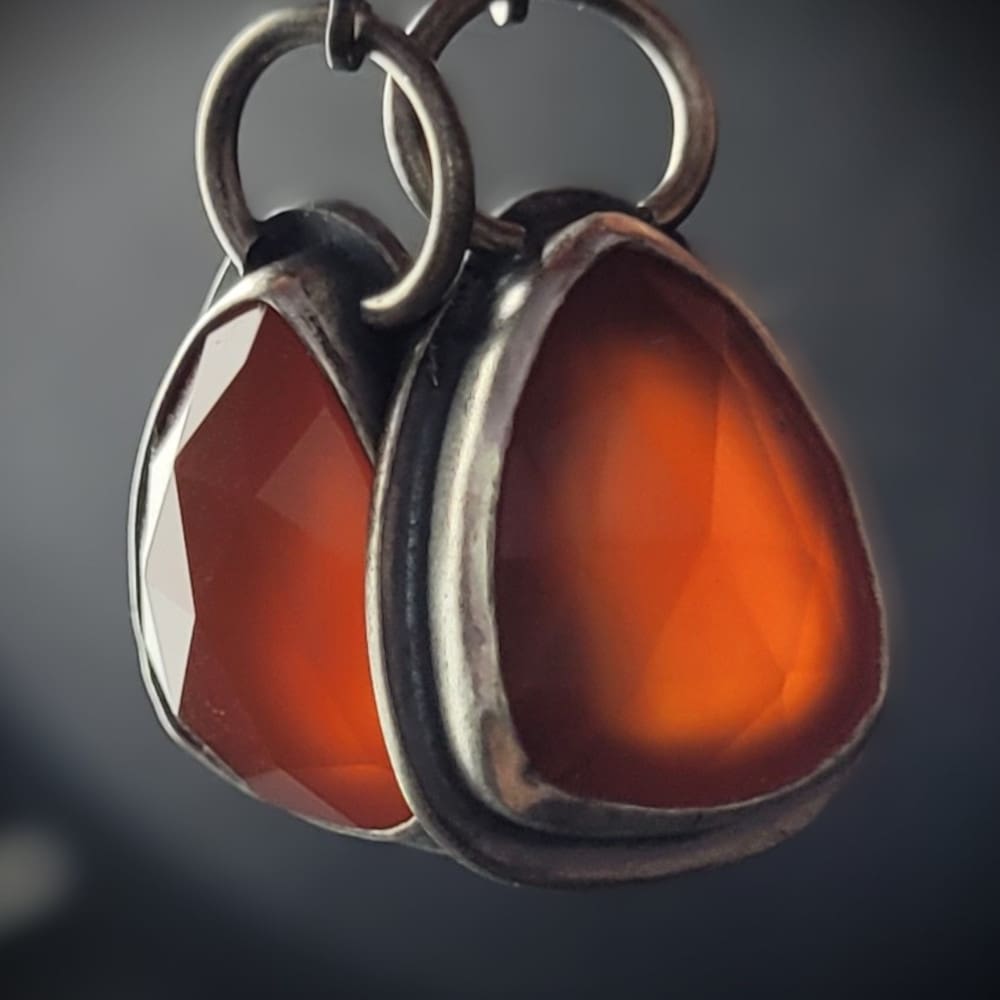 Orange Carnelian Faceted Cabochons in a raw oxidised sterling silver setting. In a teardrop shape with the back cut out to allow light through.