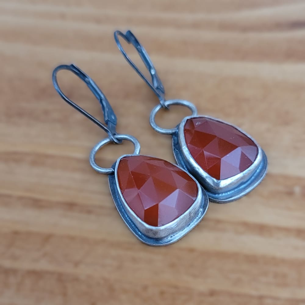 Orange Carnelian Faceted Cabochons in a raw oxidised sterling silver setting. In a teardrop shape with the back cut out to allow light through.