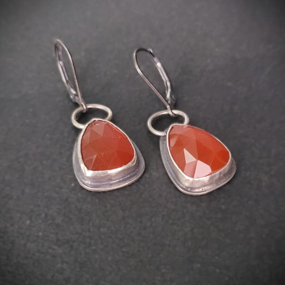 Orange Carnelian Faceted Cabochons in a raw oxidised sterling silver setting. In a teardrop shape with the back cut out to allow light through.