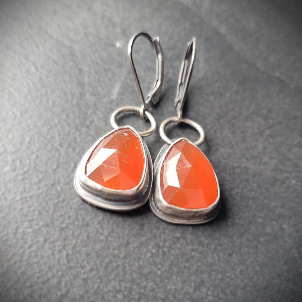 Orange Carnelian Faceted Cabochons in a raw oxidised sterling silver setting. In a teardrop shape with the back cut out to allow light through.