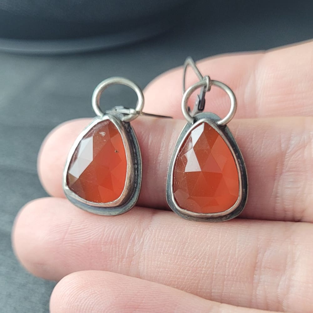 Orange Carnelian Faceted Cabochons in a raw oxidised sterling silver setting. In a teardrop shape with the back cut out to allow light through.