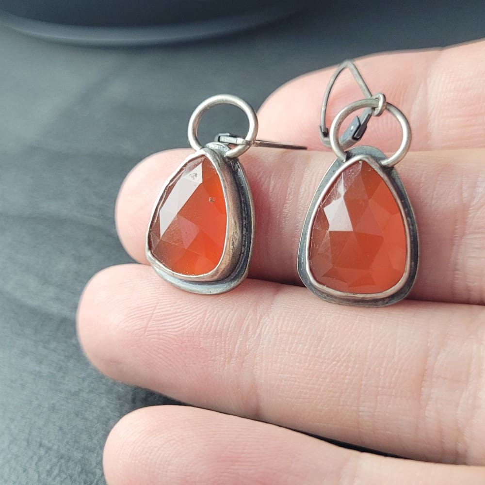 Orange Carnelian Faceted Cabochons in a raw oxidised sterling silver setting. In a teardrop shape with the back cut out to allow light through.