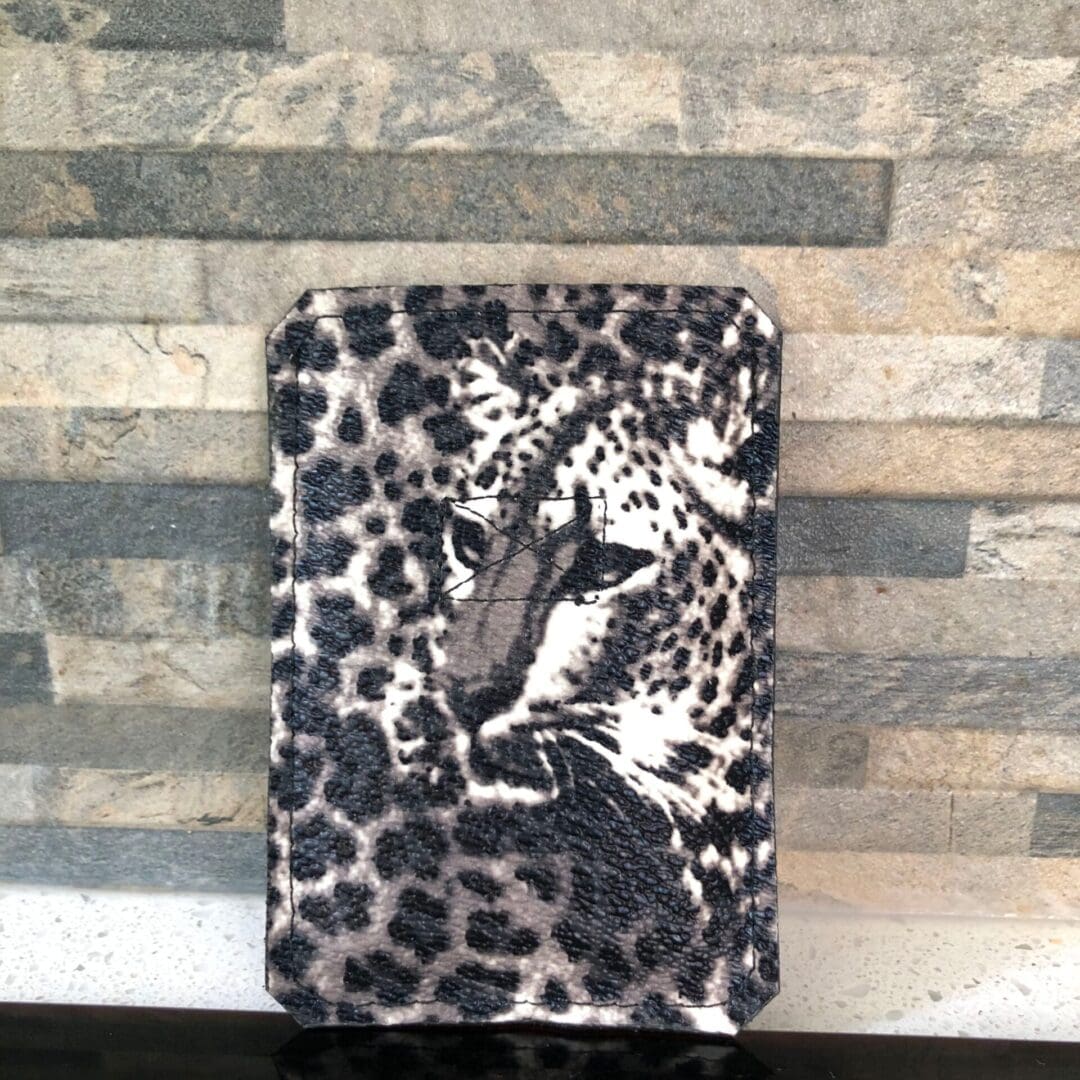 Pull tab card wallet in leopard print vinyl against a narrow brick wall