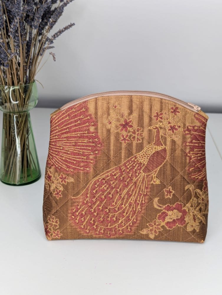 A gold and red wash bag with a peacock design