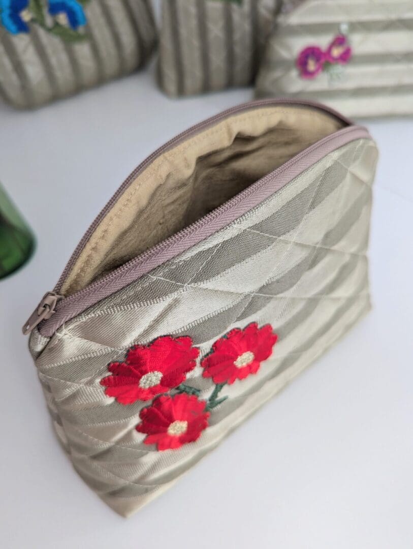 A gold make up pouch with three red flowers on one side