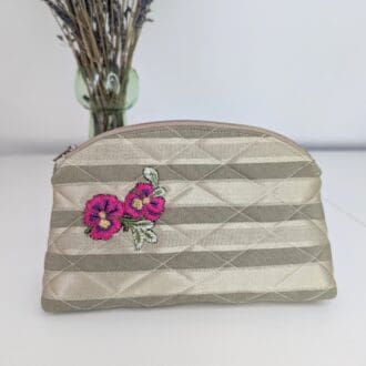 A pretty gold, quilted make up pouch with a pink floral embellishment on one side