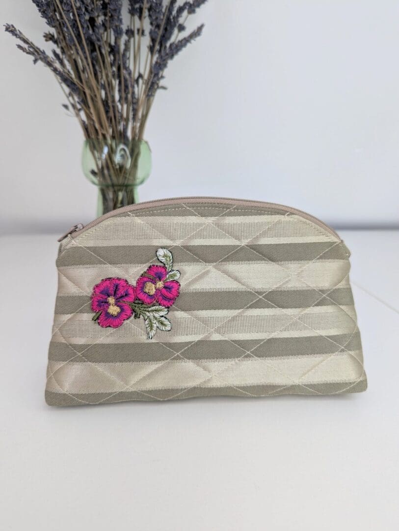 A pretty gold, quilted make up pouch with a pink floral embellishment on one side