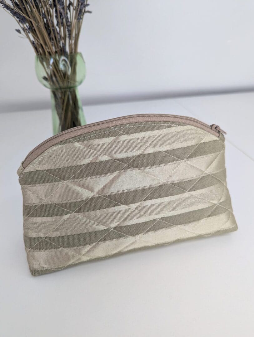 A small size make up pouch in gold striped fabric with a curved top zip