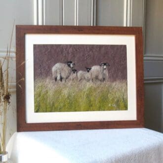 A handmade wool painting of two Swaledale sheep with two lambs stood on the horizon of a field with a dark grey sky behind them. The frame is dark wood effect and the mount is cream.