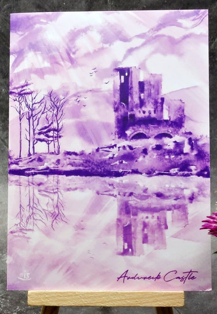 Larger image titled Ardvreck Castle showing an A6 size greetings card, blank inside, on a small easel depicting a view of Ardvreck Castle on Loch Assynt, Sutherland in purple watercolour.