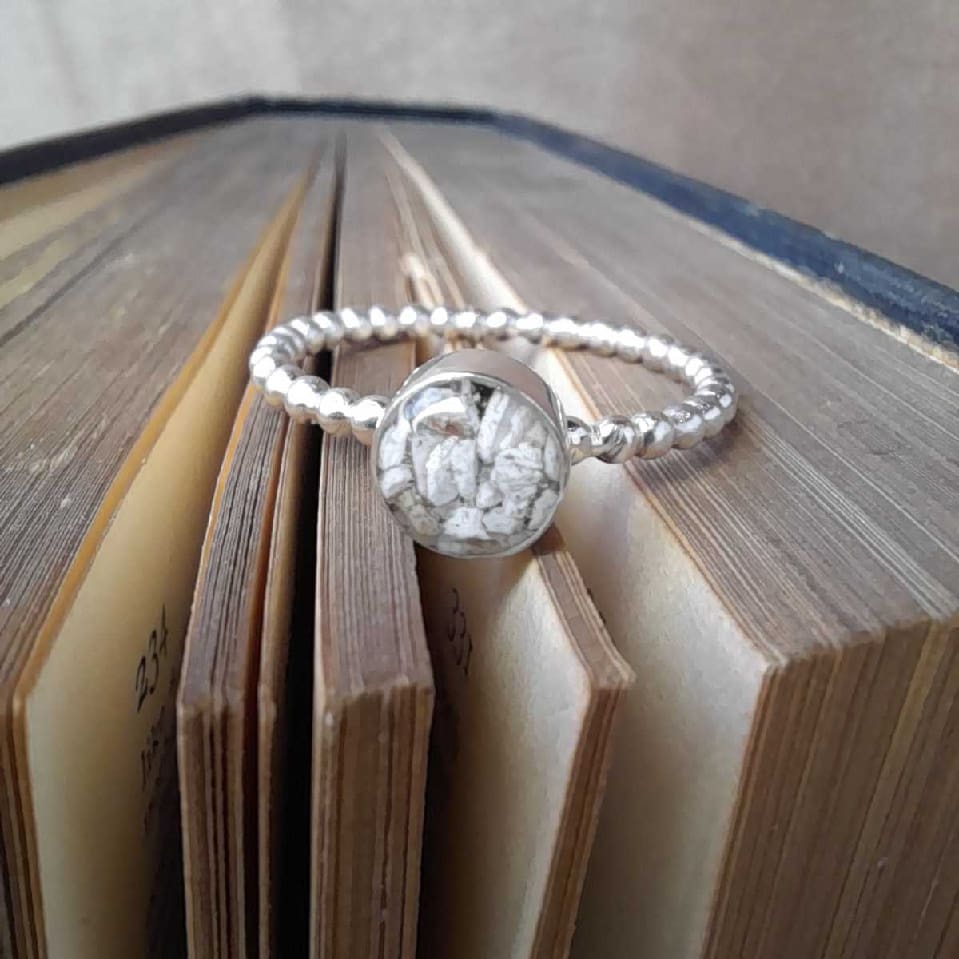 Handcrafted recycled sterling silver keepsake ring with clear resin setting including memorial ashes piece displayed on book