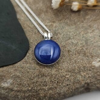 Handcrafted sterling silver domed pendant on chain, with deep blue resin stone containing ashes, displayed on soft stone